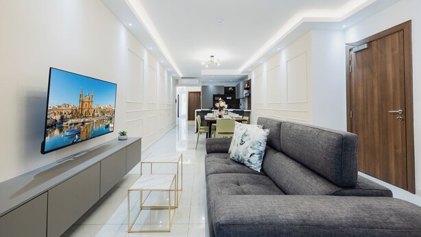 Ein modernes Wohnzimmer mit grauem Sofa, einem flachbildfernseher an der Wand und einem Essbereich im Hintergrund.