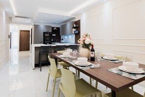 Un comedor moderno con una mesa de madera dispuesta para cuatro personas, una cocina al fondo y un florero con flores sobre la mesa.