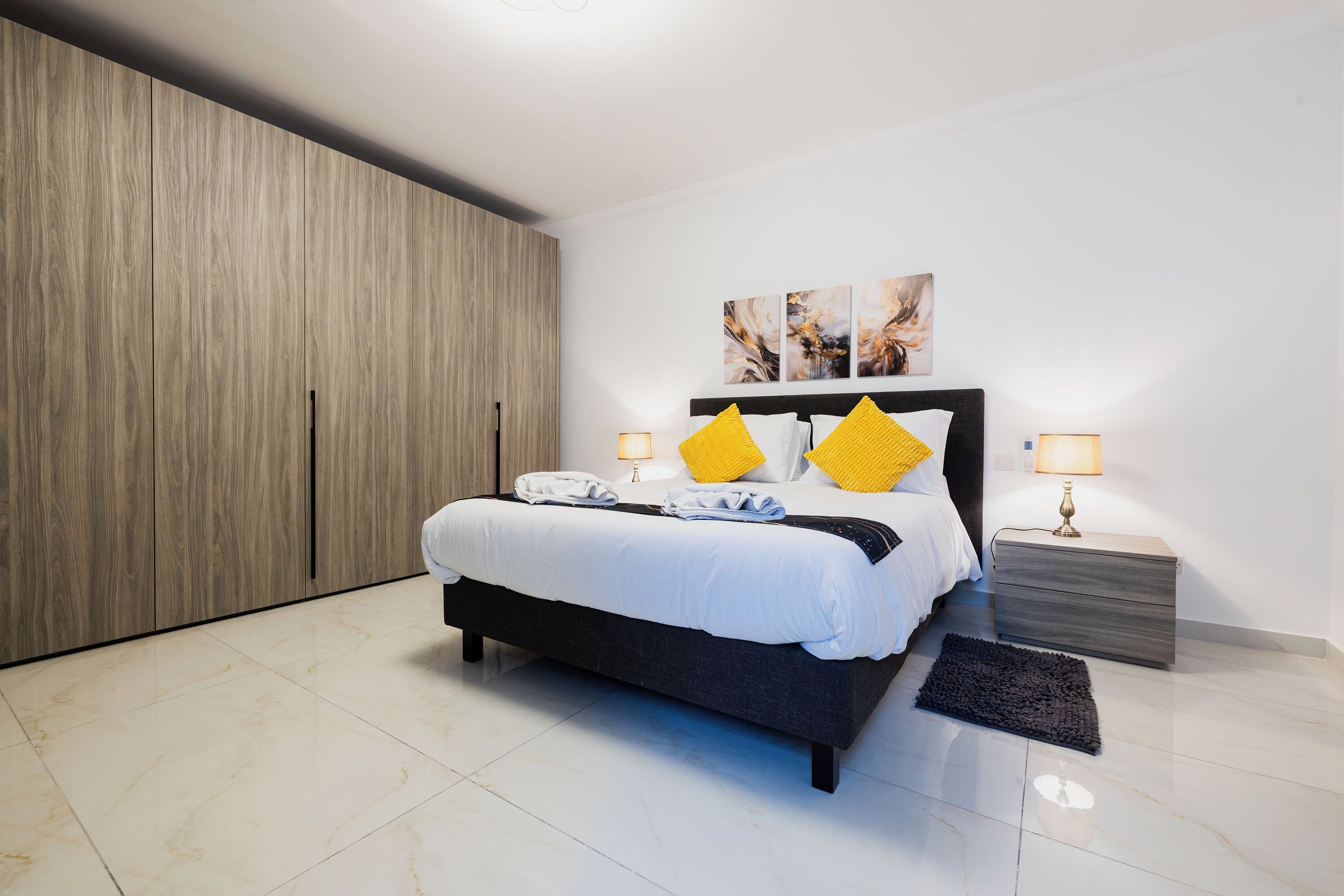Une chambre à coucher moderne avec un grand lit, une armoire en bois et des œuvres d’art accrochées au mur.