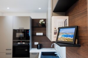 Una cocina moderna con horno empotrado, cafetera y un cuadro de un paisaje costero en la pared.