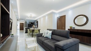 Ein modernes Wohnzimmer mit einem grauen Sofa, einem kleinen weißen Couchtisch und einem Essbereich im Hintergrund.