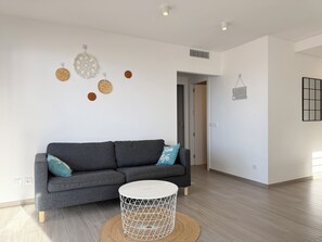 A modern living room with a grey sofa, a round coffee table, and wall decorations including circular woven items and a geometric wall art piece. - Agi Residencial Roses 215 Apartamento for rent in Roses Girona. (Roses)