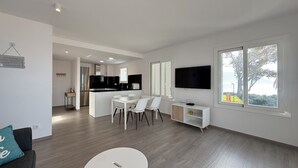 En moderne stue med spiseplads, et køkken og et tv ophængt på væggen.