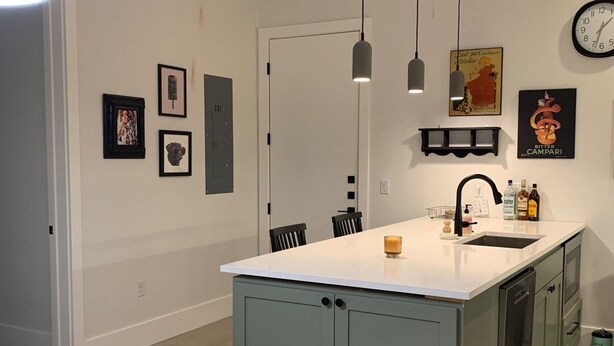 A modern kitchen with a central island, pendant lights, a clock, and framed artwork on the walls. - Beautiful New Construction 2 - Bedroom / 2 Bath located in West University. (Austin)