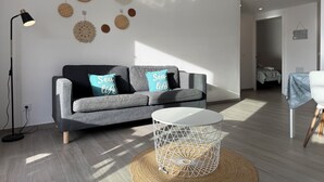 Uma sala de estar moderna com um sofá cinza, duas almofadas com a inscrição 'Sea life', uma mesa de centro branca redonda e um abajur de chão.