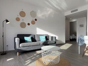 A modern living room with a grey sofa, two pillows with 'Sea life' text, a round white coffee table, and a floor lamp. - Agi Residencial Roses 201 Apartamento for rent in Roses Girona. (Roses)