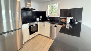 Cozinha moderna com eletrodomésticos de aço inoxidável, bancada preta e janela com vista para o verde.