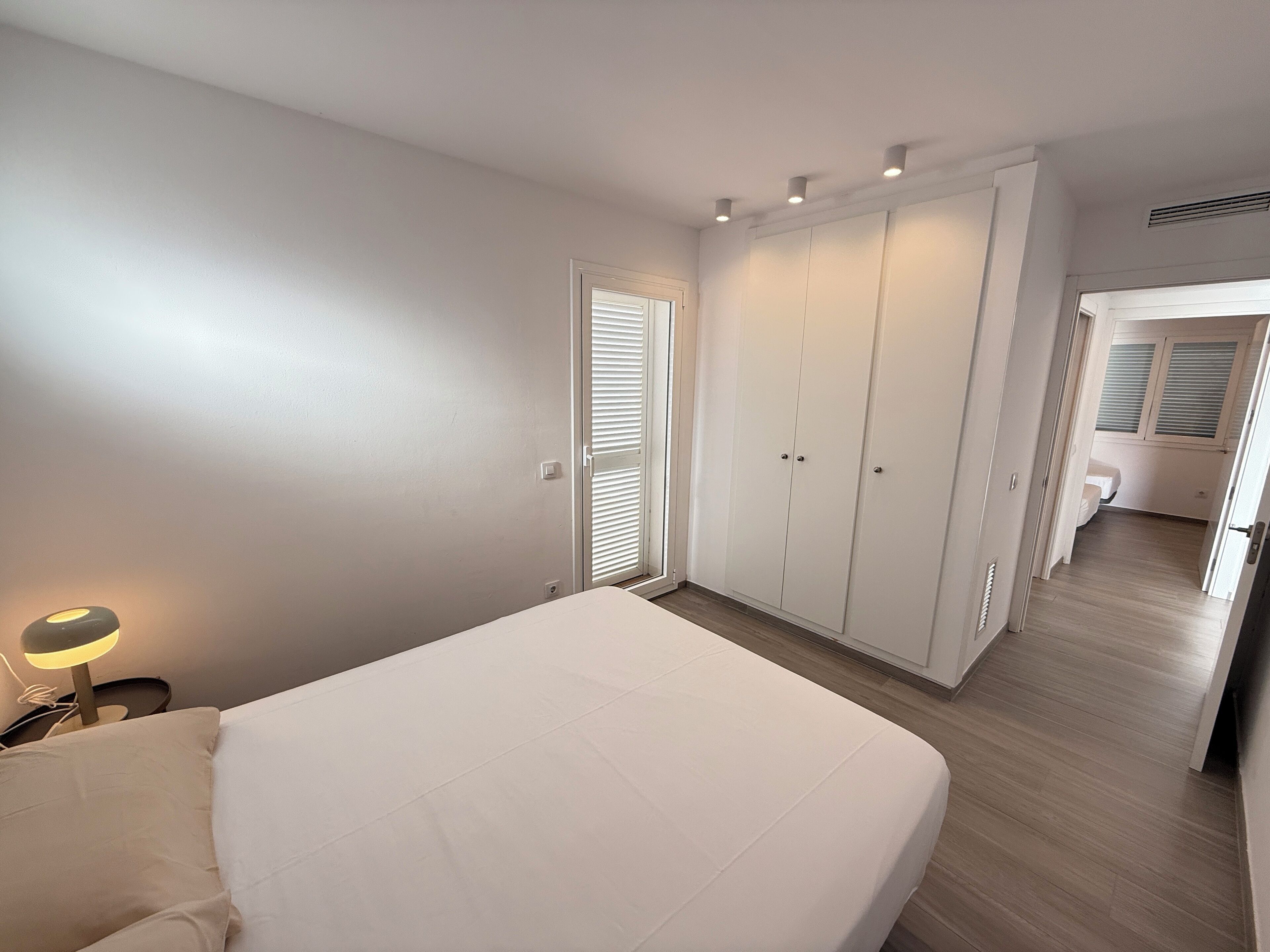 A bedroom with a bed, a nightstand, a wardrobe, and a door leading to another room.