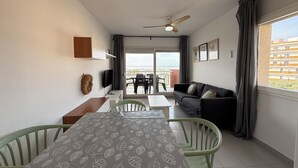 Un salon moderne comprenant un coin repas, un ventilateur de plafond, un téléviseur et un balcon offrant une vue sur la ville.