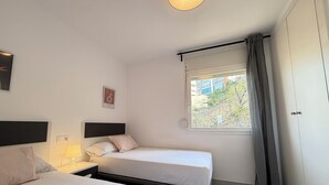 Une chambre d’hôtel avec deux lits, une fenêtre avec des rideaux, un lampadaire fixé au mur et un tableau encadré.