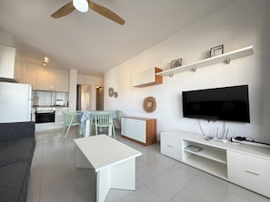 A modern living room with a flat-screen TV, a dining area with a table and chairs, and a kitchen in the background. - Agi Rocmar 134 Apartamento for rent in Roses Girona. (Roses)