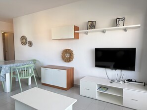 A modern living room with a TV, white cabinets, a dining table with chairs, and decorative wall art. - Agi Rocmar 134 Apartamento for rent in Roses Girona. (Roses)