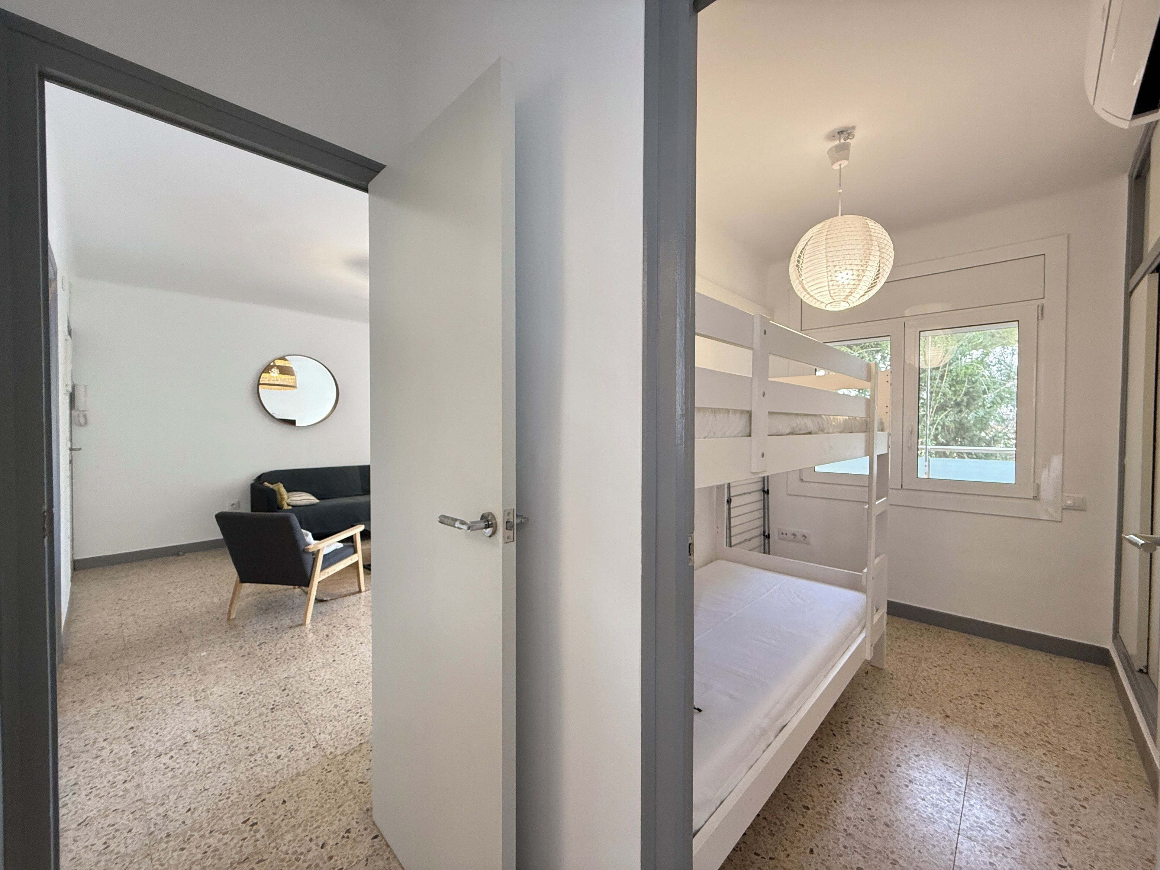 A modern bedroom with a bunk bed, a bedside table, a chair, a mirror, and a hanging light fixture.