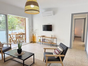 Ein Wohnzimmer mit Fernseher, einer Pflanze, einer Couch, einem Couchtisch und einem Essbereich mit Stühlen und einem Tisch.