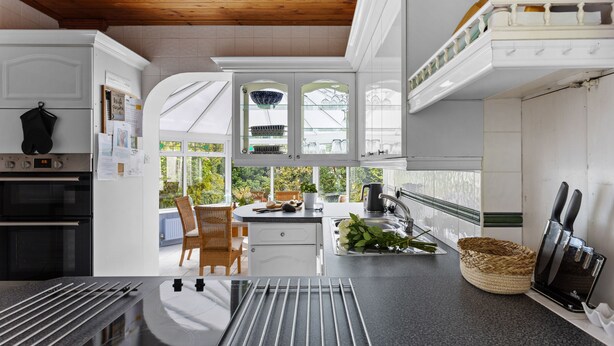 A modern kitchen with white cabinetry, a black countertop, and a wooden ceiling. - Blue Haze (St Austell)