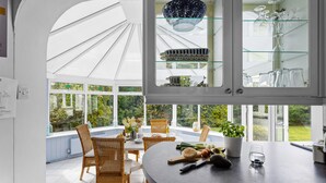 A kitchen with a round island, wicker chairs, a dining table, and a glass cabinet with kitchenware. - Blue Haze (St Austell)