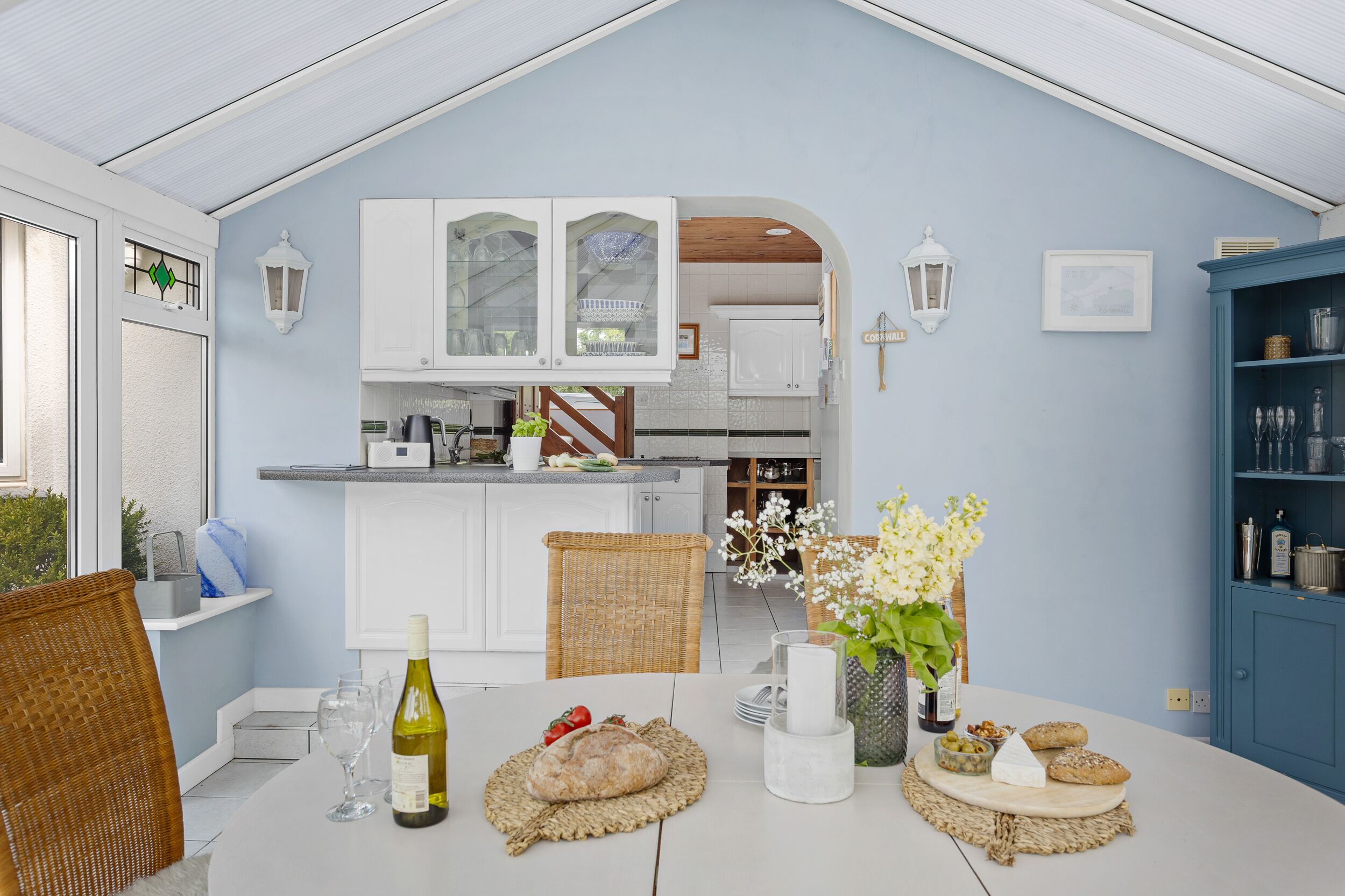 A kitchen with white cabinets, a dining table with a bottle of wine, bread, and flowers.