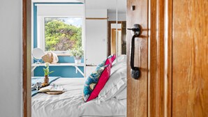 A bedroom with a bed, pillows, a bedside table, and a window. - Blue Haze (St Austell)