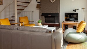 Un salon moderne avec un canapé, des fauteuils jaunes, une cheminée, un téléviseur et un escalier en colimaçon.
