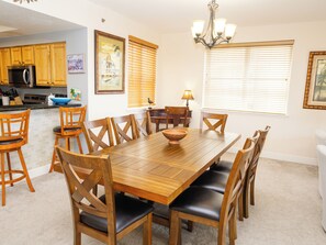Een eetgedeelte met een houten tafel en stoelen, een keuken op de achtergrond en een kroonluchter.