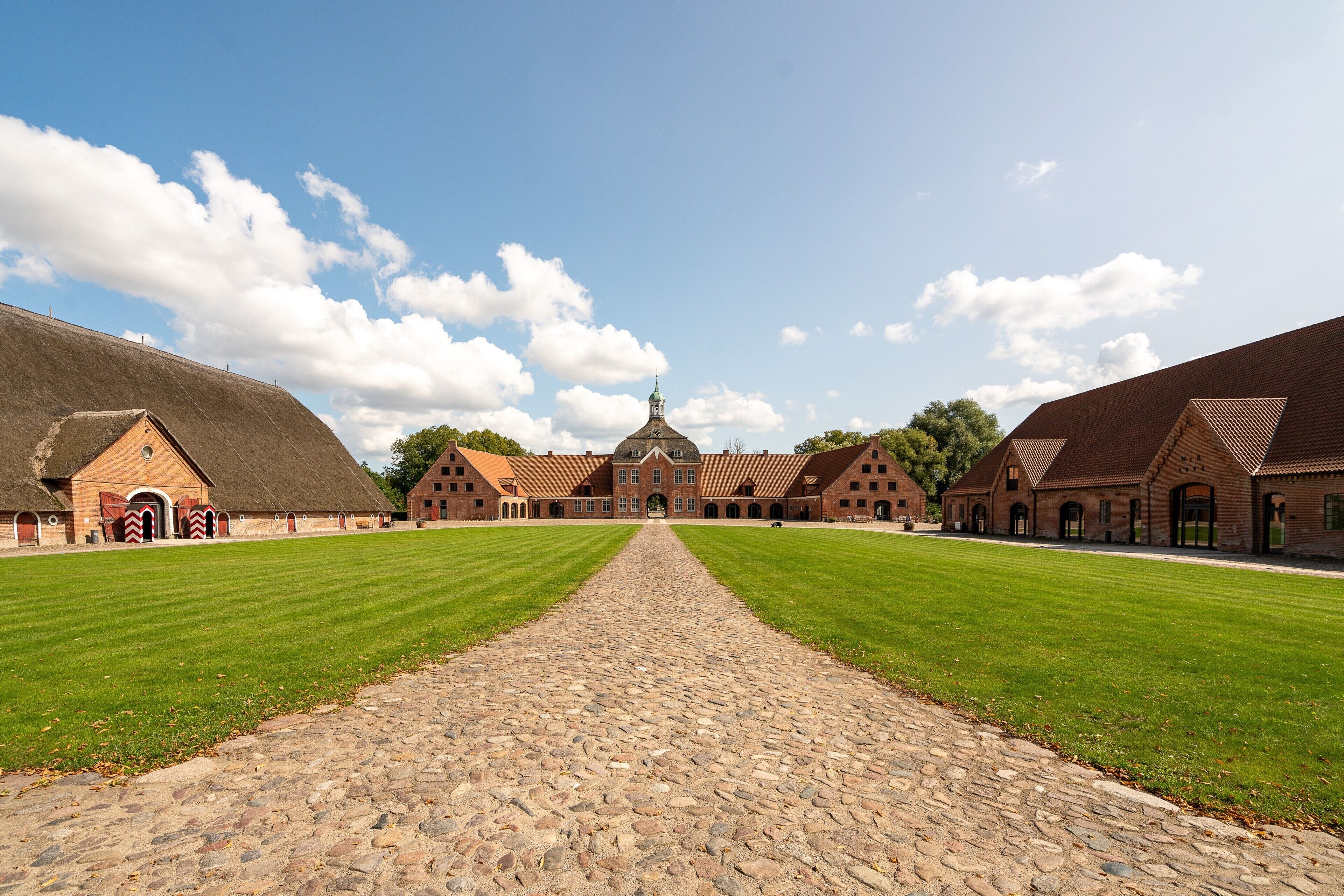 A courtyard with a cobblestone path leading to a large building with a central dome and multiple smaller structures.