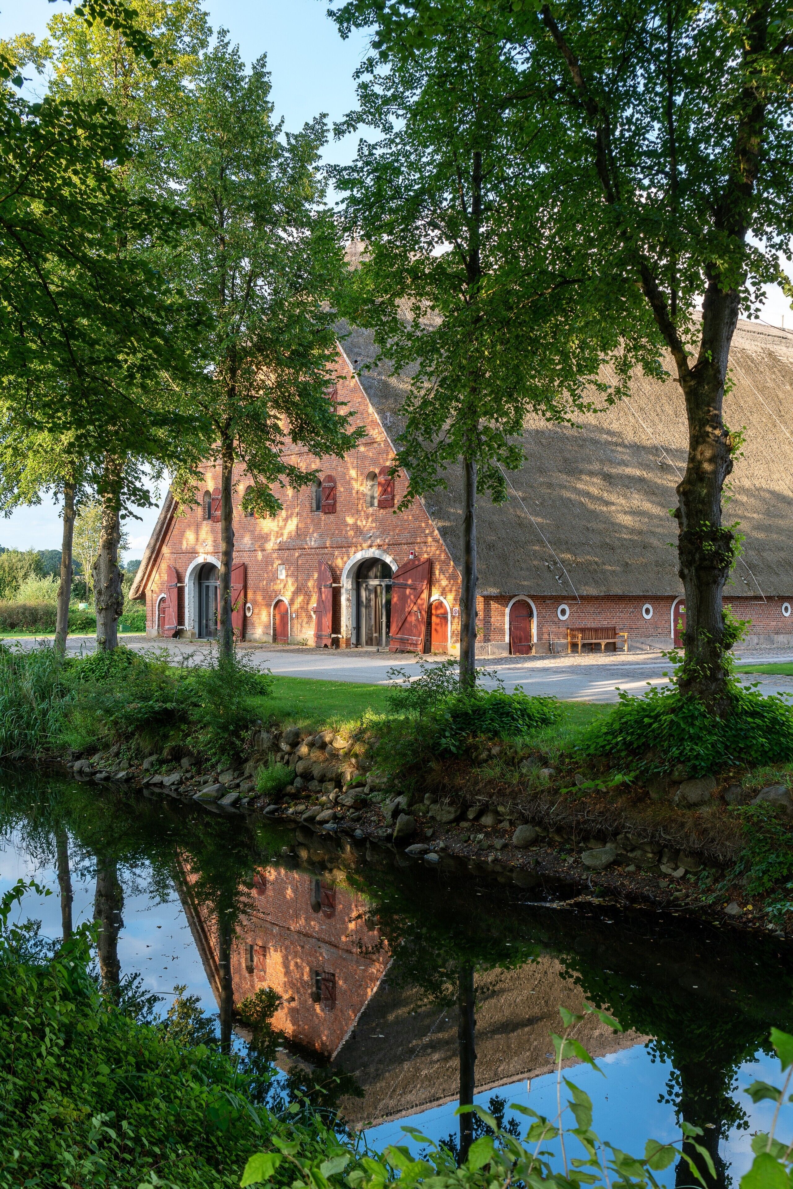 A brick building with arched doorways and a reflection in a calm body of water.