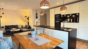Een moderne keuken met een centraal eiland, hangende verlichting en een eethoek met een houten tafel en witte stoelen.