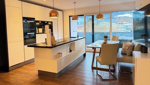 Een moderne keuken met een centraal eiland, een eethoek met tafel en stoelen, en grote ramen met uitzicht op de stad.