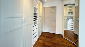 Een hal met een houten vloer, witte kasten met schuifdeuren en een spiegel aan de rechterwand.