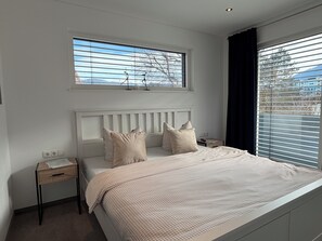 Ein Schlafzimmer mit einem Bett, einem Nachttisch, einem Fenster und Blick ins Freie.