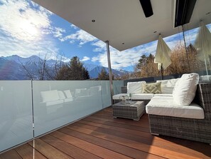 Un balcón con piso de madera, baranda de vidrio y un sofá con cojines.