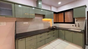Una cocina moderna con armarios verdes, encimera negra y salpicadero de azulejos.