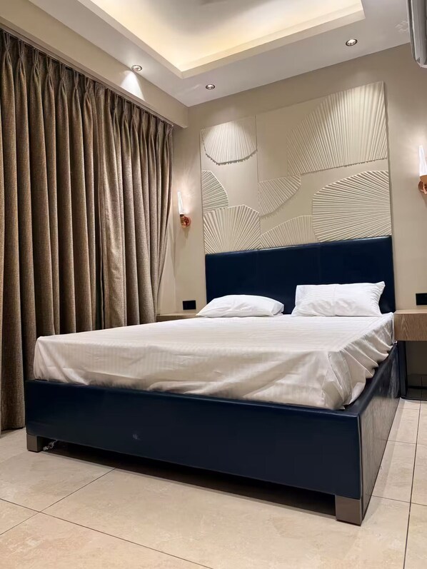 A modern bedroom with a dark blue bed, beige curtains, and a wall with a geometric pattern.