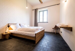 Une chambre à coucher avec un lit en bois, une table de chevet, une chaise, une fenêtre avec des rideaux et une étagère avec des serviettes.