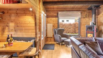 A wooden cabin interior with a dining table, cushioned seating, a fireplace, and a large window.
