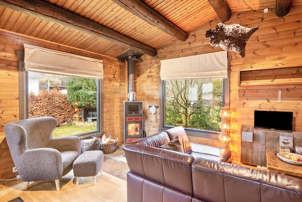 Ein gemütliches Holzinterieur mit Kamin, Ledersofa und einem großen Fenster mit Blick auf einen Garten.