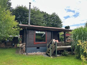 Ein rustikales Blockhaus mit Schornstein, einem Fenster und einer Holztreppe, die zu einer Veranda führt.