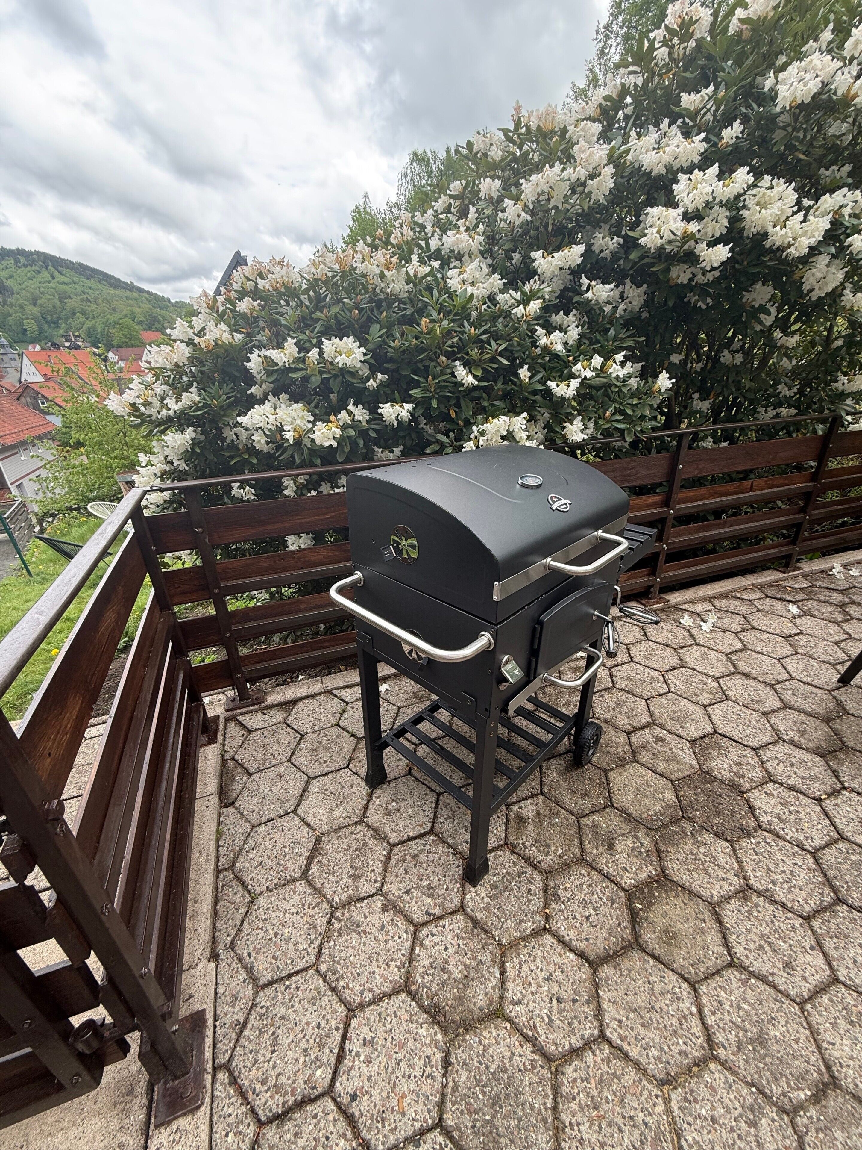 Ein Grill auf einer sechseckigen Terassenfliese mit Holzlattenzaun und einer Bank.