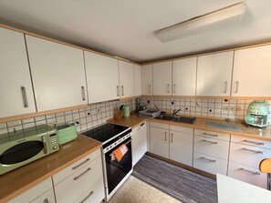 A kitchen with white cabinets, a stove, a microwave, and a sink.
