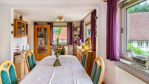 Comedor con una mesa larga, sillas, una lámpara de araña y vista a una casa a través de la ventana.