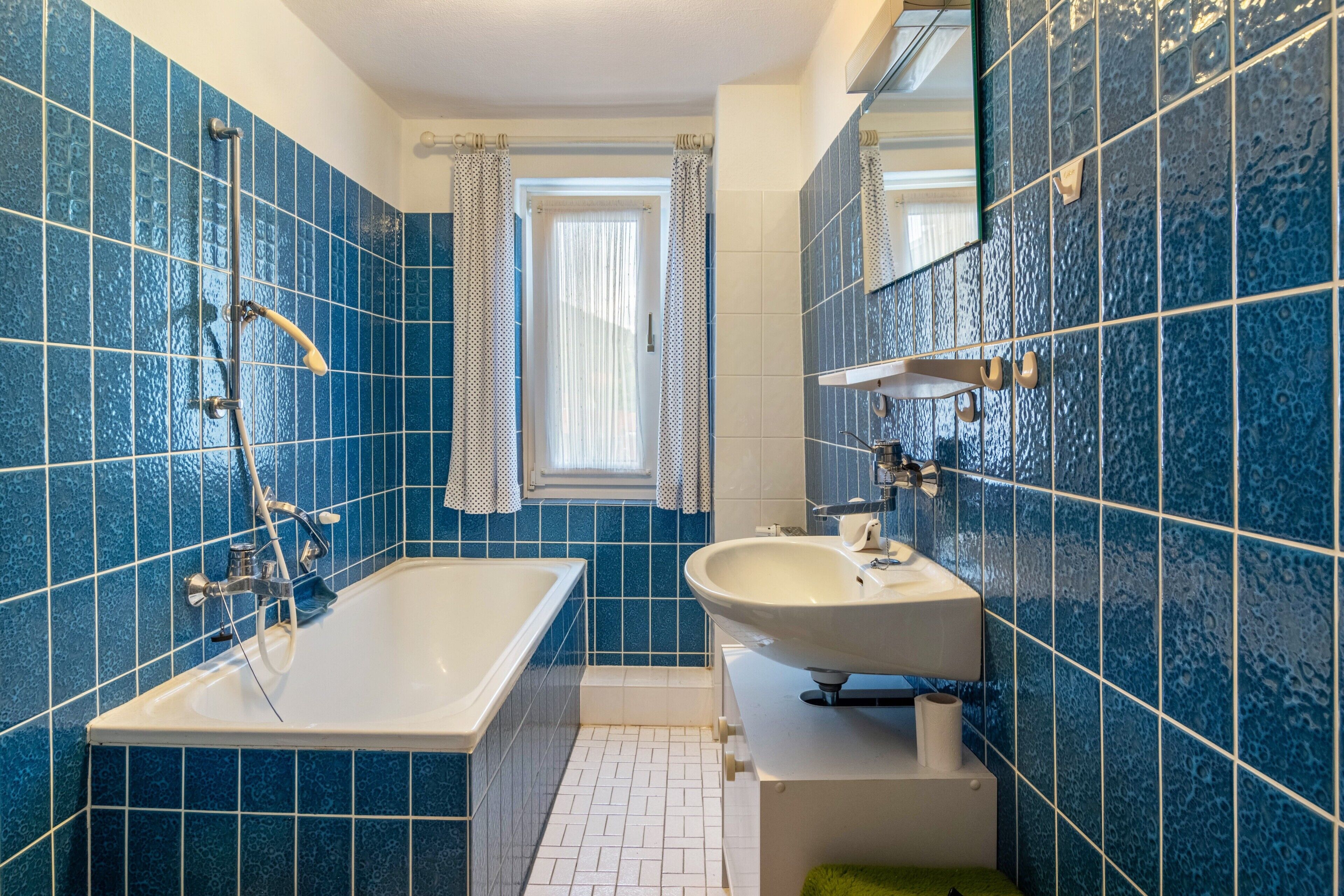 A bathroom with a bathtub, a sink, and a window with curtains.