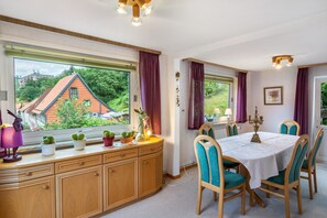 A dining area with a table set for four, wooden cabinets, and a view of a red-roofed building through large windows.