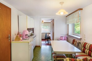 A compact kitchen with a dining area, a window with lace curtains, and a radiator.