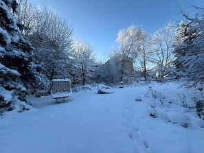 Schneebedecktes Freigelände mit einer Bank und einem Gebäude im Hintergrund.