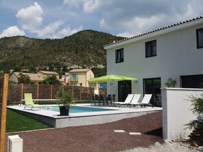 A modern building with a swimming pool, outdoor seating, and a view of a mountainous landscape. - Modern vacation villa with heated private pool in the most beautiful region of France (Castellane)