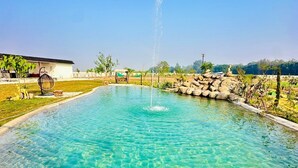 Ein klarer, runder Pool mit einer zentralen Fontäne, umgeben von einer Steinmauer und Pflanzen.
