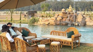 A serene outdoor seating area with wicker furniture and a large umbrella, overlooking a pond with a Buddha statue and a rock formation. - Countryside Heaven Farm (Kharar)