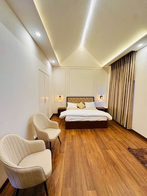 Una camera d'albergo moderna con un letto grande, due poltrone, pavimento in legno e un soffitto con faretti.