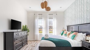 Une chambre à coucher avec un lit, une commode, une télévision et une fenêtre avec des rideaux.
