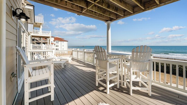 Une terrasse en bois avec des fauteuils Adirondack blancs donnant sur l’océan.